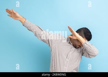 Portrait de l'homme d'affaires anonyme debout mains levées dans dab danse pose, mémoire Internet, célébrant le succès, portant une chemise rayée. Studio d'intérieur isolé sur fond bleu. Banque D'Images