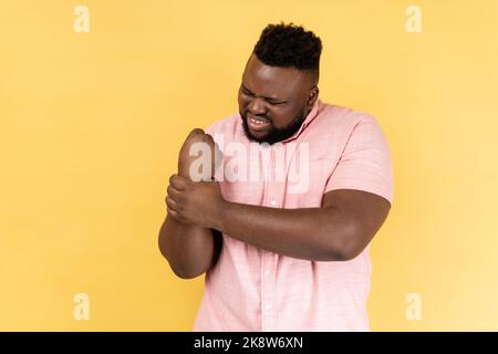 Entorse de poignet. Portrait d'un homme portant une chemise rose touchant la main blessée grimaquant dans la douleur, souffrant du syndrome du tunnel carpien, arthrite inflammation. Studio d'intérieur isolé sur fond jaune. Banque D'Images