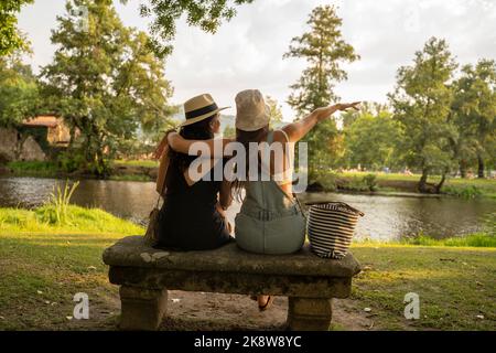 deux filles amies avec chapeaux discutant assis sur un banc de pierre en face de la rivière Banque D'Images