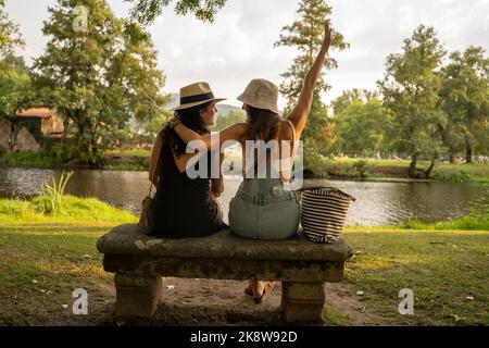 deux filles amies avec chapeaux discutant assis sur un banc de pierre en face de la rivière Banque D'Images