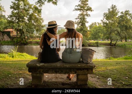 deux filles amies avec chapeaux discutant assis sur un banc de pierre en face de la rivière Banque D'Images