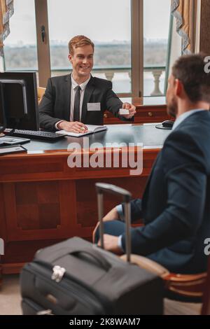 Homme d'affaires avec bagguge est d'enregistrer dans un hôtel de luxe et de recevoir la carte-clé de la réceptionniste Banque D'Images