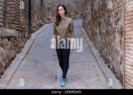 Jeune femme voyageant avec une chemise militaire verte marchant dans une rue étroite d'une ville médiévale Banque D'Images