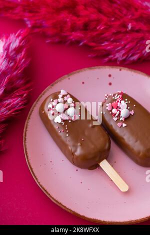 Cupcake à la crème glacée.Cupcakes au chocolat sur une assiette rose avec des fleurs séchées roses sur un fond de fuchsia brillant.biscuits au chocolat sur un bâton Banque D'Images