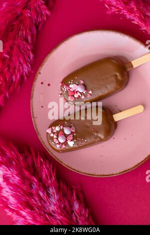 Cupcakes au chocolat sur une assiette rose avec fleurs séchées roses sur un fond de fuchsia brillant.vue d'en haut.biscuits au chocolat sur un bâton dans le Banque D'Images
