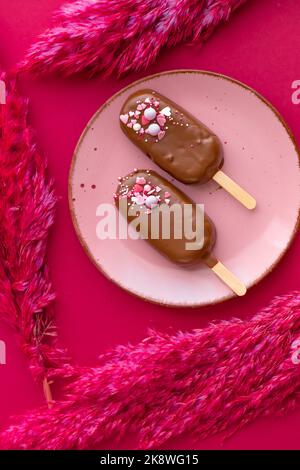 Crème glacée à base de cupcake et crème au chocolat. Petits gâteaux au chocolat sur une assiette rose avec fleurs séchées roses sur un fond de fuchsia brillant. Vue d'en haut Banque D'Images