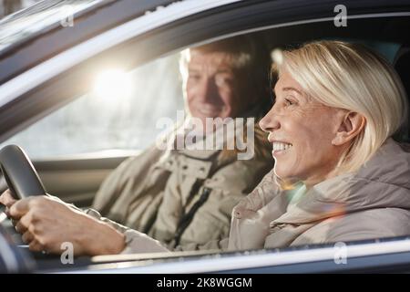 Portrait de vue latérale d'un couple de personnes âgées gaies conduisant une voiture en hiver, concentrez-vous sur une femme souriante derrière le volant, espace de copie Banque D'Images