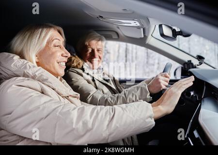 Portrait de vue latérale d'un couple senior joyeux conduisant une voiture en hiver et essayant de réchauffer les mains sur le chauffage de la voiture, espace de copie Banque D'Images