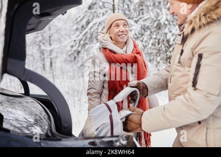 Portrait d'un couple d'âge mûr profitant d'une escapade hivernale dans la nature debout en voiture avec le coffre ouvert Banque D'Images