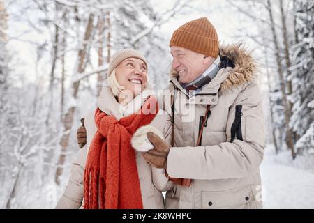 Portrait de la taille vers le haut de couple heureux de personnes âgées en appréciant la promenade dans la forêt d'hiver et regardant l'un l'autre avec amour Banque D'Images