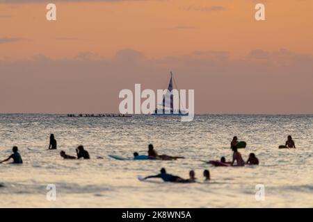 Superbe coucher de soleil au départ d'Oahu à Hawaï avec silhouettes de surfeurs et nageurs. Banque D'Images