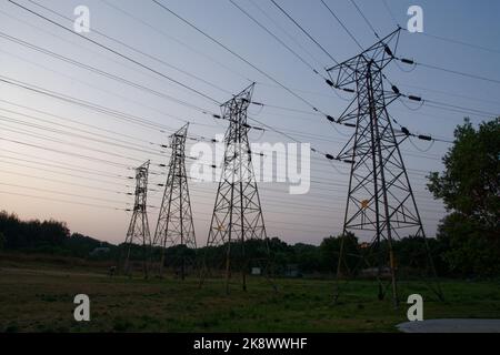 Quatre câbles électriques au pavillon Pylons silhouetés contre le ciel de la soirée. Dans un paysage rural Banque D'Images