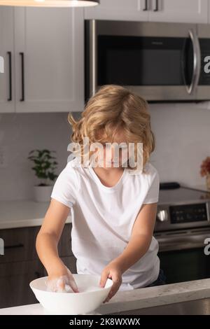 Vaisselle de nettoyage pour enfants avec éponge. Fournitures de nettoyage. Aide au nettoyage. Tâches d'entretien ménager. Vaisselle de lavage pour enfants. Un petit garçon mignon lave les plats près de l'évier Banque D'Images