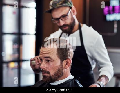 La satisfaction de la clientèle est notre priorité. Un homme mûr et beau qui obtient une coupe de cheveux dans un salon de coiffure. Banque D'Images