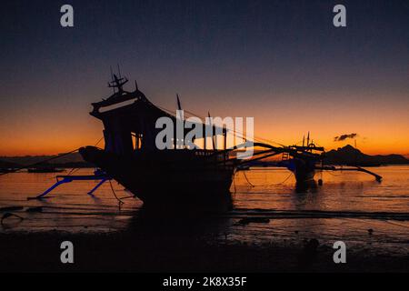 Silhouette de bateaux traditionnels des philippines sur fond de coucher de soleil. Soirée calme en bord de mer en Asie. Bateaux de pêche le soir au crépuscule avec l'île. Banque D'Images