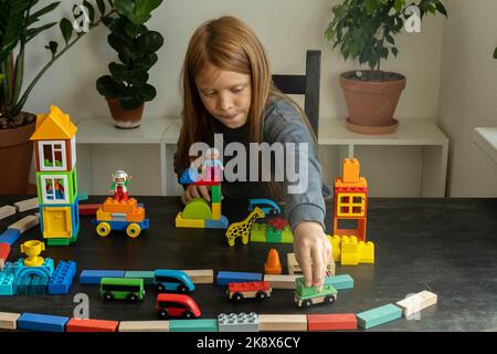 Le garçon de 8 ans joue des cubes et des blocs . Il a construit une ville et un chemin de fer. Activités de loisirs et loisirs à la maison. Un petit inventeur. Photo horizontale. Banque D'Images