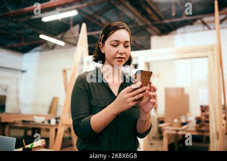 Comme notre page et bien vous donner 30 off. Une femme charpentier utilisant son téléphone cellulaire dans son atelier. Banque D'Images