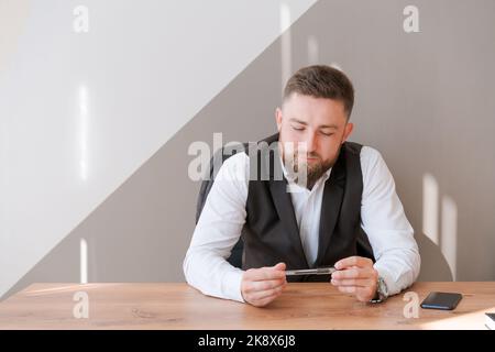 Homme d'affaires décontracté barbu, assis à la table avec un stylo dans sa main, pensant à un projet de travail, habillé dans une chemise dans le bureau. Entreprise de démarrage, concept de bureau portable Banque D'Images