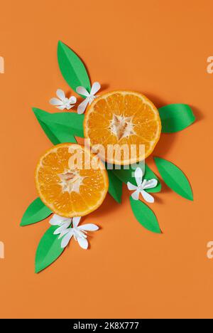 Composition créative de deux moitiés de mandarine sur fond orange, éléments de feuilles de papier et de fleurs. Banque D'Images