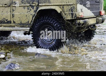 Tout-terrain sur route de montagne. Vue du bas sur une grande roue de voiture sur la route de campagne et la toile de fond des montagnes. Concept de voyage avec grande voiture 4x4. Banque D'Images