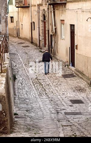 Homme aîné avec chapeau coppola et canne à pied sur la rue en pierre du village médiéval de Prizzi en Sicile occidentale, Italie Banque D'Images