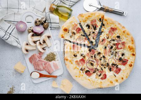 Pizza au bacon et aux champignons sur une table à côté des ingrédients crus. Vue de dessus. Banque D'Images