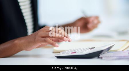 Tenir au budget est la partie délicate. Une femme d'affaires méconnaissable travaillant ses finances avec une calculatrice et un bloc-notes dans son bureau. Banque D'Images