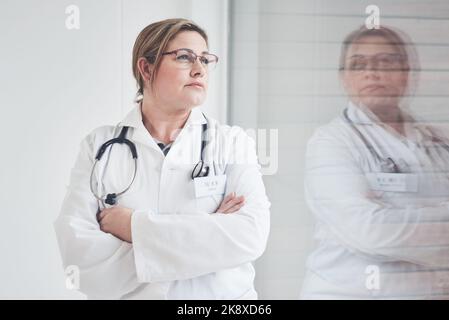 Il y a beaucoup à réfléchir. Une jeune femme médecin attirante qui a l'air réfléchie tout en se tenant debout avec ses bras croisés dans son bureau. Banque D'Images