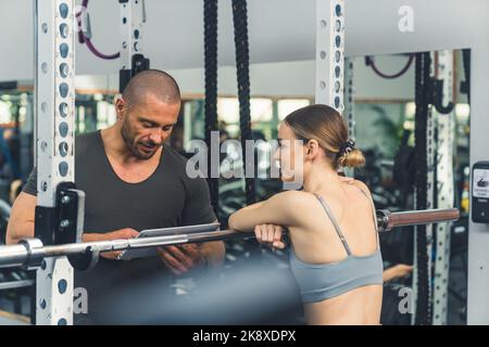 Jeune fille fine et attrayante de race blanche dans son 20s à l'écoute de son instructeur personnel privé donnant son feedback après le test de force. Gros plan moyen, intérieur de la salle de sport. Photo de haute qualité Banque D'Images