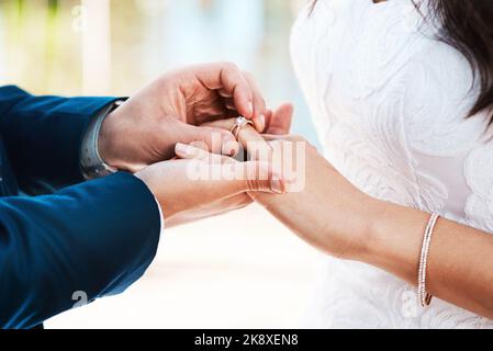 Mon amour pour vous brille brillant comme un diamant. Un marié méconnaissable glissant un anneau sur son doigt de mariée tout en se tenant debout à l'extérieur sur leur mariage Banque D'Images