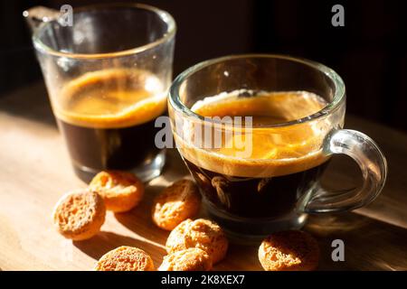 Deux tasses transparentes d'espresso italien sur une surface en bois avec petits biscuits. Photo à contraste élevé le matin. Arrière-plan flou Banque D'Images