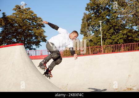 L'homme énergique sur le roller skate en mouvement dans le parc de roller moderne. Patineuse à roulettes faisant des tours dangereux et audacieux. Sport, santé, vitesse et Banque D'Images