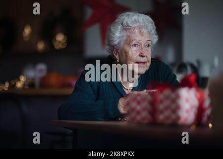 Femme âgée malheureuse assise seule et attendant sa famille pendant la veille de Noël.concept de solitude, de santé mentale et de sénior. Banque D'Images
