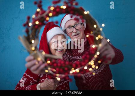 Portrait d'un couple senior heureux avec chapeaux du Père Noël en studio, en regardant la couronne de Noël. Banque D'Images