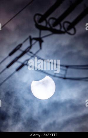 Cologne, Allemagne. 25th octobre 2022. Le soleil éclipsé par la lune brille à travers une couverture nuageuse. Au premier plan, les isolateurs d'une ligne haute tension sont visibles. Credit: Henning Kaiser/dpa/Alay Live News Banque D'Images