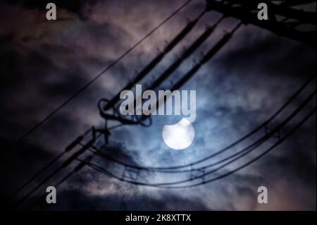 Cologne, Allemagne. 25th octobre 2022. Le soleil éclipsé par la lune brille à travers une couverture nuageuse. Au premier plan, les isolateurs d'une ligne haute tension sont visibles. Credit: Henning Kaiser/dpa/Alay Live News Banque D'Images