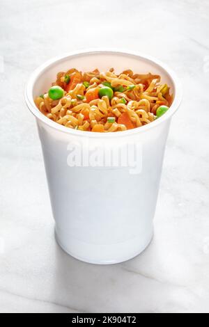 Coupe de ramen, nouilles soba instantanées dans une tasse en plastique avec légumes, oignons verts, petits pois et carottes, sur une table en marbre blanc Banque D'Images