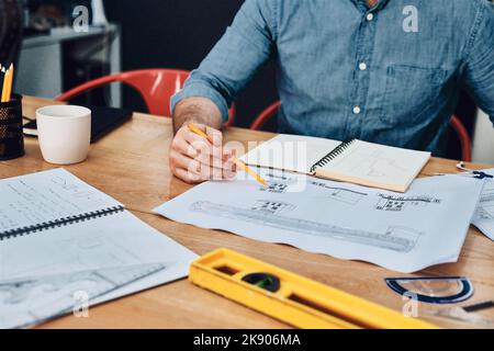 C'est sa chose de concevoir. Un architecte masculin méconnaissable travaillant avec des plans dans un bureau moderne. Banque D'Images