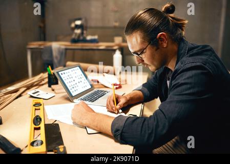 Il a des compétences de niveau supérieur. Un jeune menuisier de sexe masculin qui travaille sur un projet à l'intérieur d'un atelier la nuit. Banque D'Images