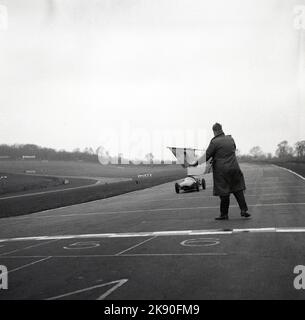 1959, historique, course automobile, sur le circuit de courses automobiles de Brands Hatch, pilote d'école de course dans une Cooper Formula Junior, avec un officiel de la Cooper Driving School, sur la piste à la ligne d'arrivée avec un drapeau pour amener le pilote à Hatch Brands, Kent, Angleterre, Royaume-Uni. Banque D'Images