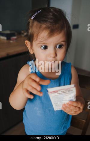 Portrait d'une adorable petite fille cuisant quelque chose de savoureux avec sa mère, lui donnant un paquet de poudre à pâte. Les enfants cuisent avec Banque D'Images