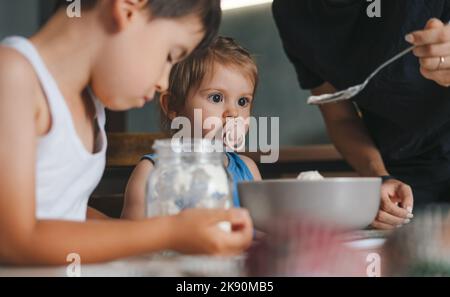 Deux enfants du caucase aidant sa mère qui pèse de la farine dans la cuisine. Concept d'activité familiale. Concept « Love People ». Bonne famille, enfance Banque D'Images