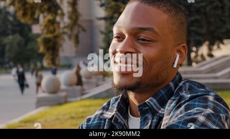 Afro-américain beau jeune homme écoutant de la musique sans fil écouteurs dans le centre-ville. Gros plan portrait multiracial Guy étudiant appréciant la chanson Banque D'Images