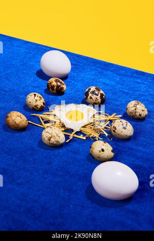 Photographie d'art pop. Composition avec caille et œufs de poulet sur nappe bleu vif isolée sur fond jaune. Style rétro, coloré Banque D'Images