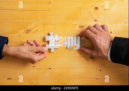 Mains de deux partenaires d'affaires, hommes et femmes, correspondant à deux pièces de puzzle vierges sur un fond jaune texturé. Banque D'Images