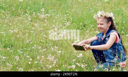 Petite fille tenant un téléphone, mobile, prenant des photos d'eux, prenant des photos d'une pelouse camomille. Photo de haute qualité Banque D'Images