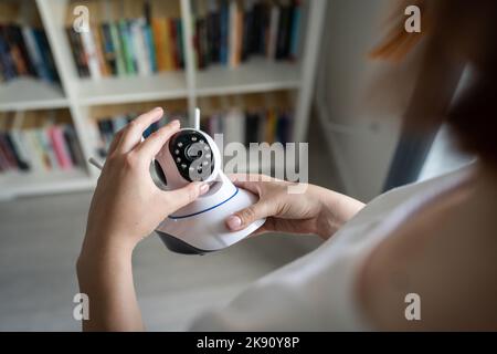 Gros plan sur la section médiane et les mains d'une femme caucasienne inconnue qui tient une caméra de surveillance de la sécurité à domicile tout en se tenant debout dans la pièce pour régler et installer Banque D'Images