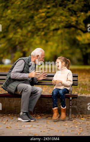 Beau grand-père jouant les mains rouges jeu de claquement avec sa petite-fille dans le parc le jour de l'automne Banque D'Images