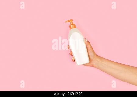 Femme tenant main un distributeur de savon sur fond rose avec espace de copie Banque D'Images