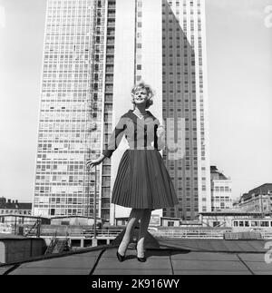 Dans le 1950s. Une femme qui se moque d'une tenue de 1950s avec une veste et une jupe dans le noir assorti. En arrière-plan, le gratte-ciel récemment terminé abrite les bureaux fiscaux suédois. Suède 1959 Kristoffersson réf. CH21 Banque D'Images